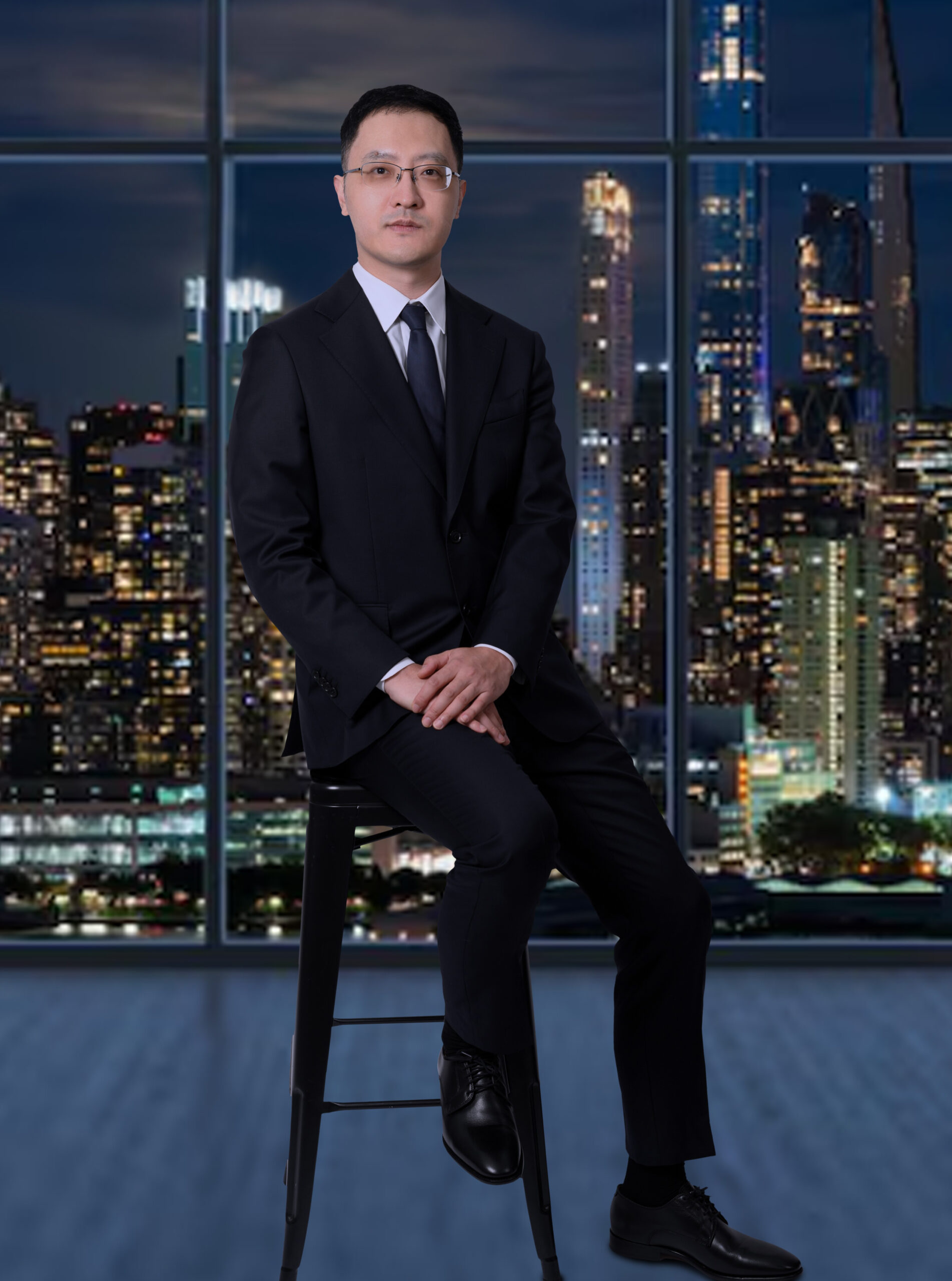 Mr. Yunfei (Alan) Ni, Chief Counsel of Ni Law, sitting on a stool with a beautiful nighttime scene of Hong Kong behind him.